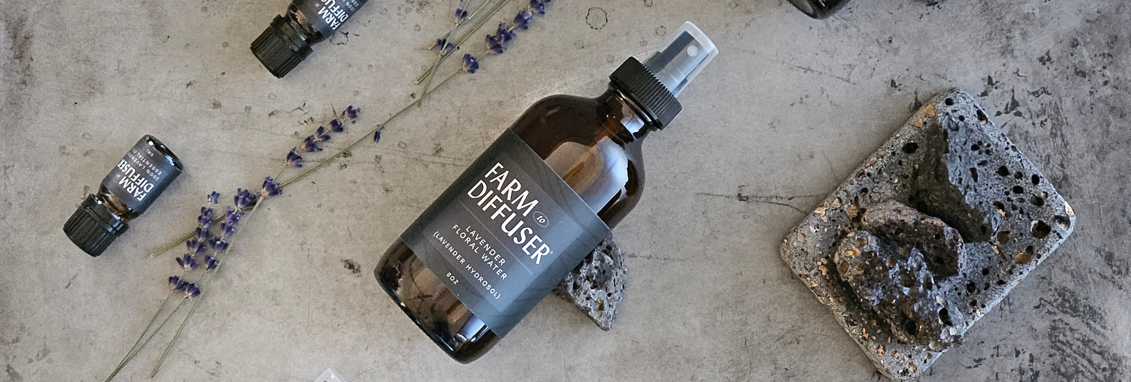 Farm Diffuser hydrosol bottles on a textured surface with lavender flowers and volcanic rocks