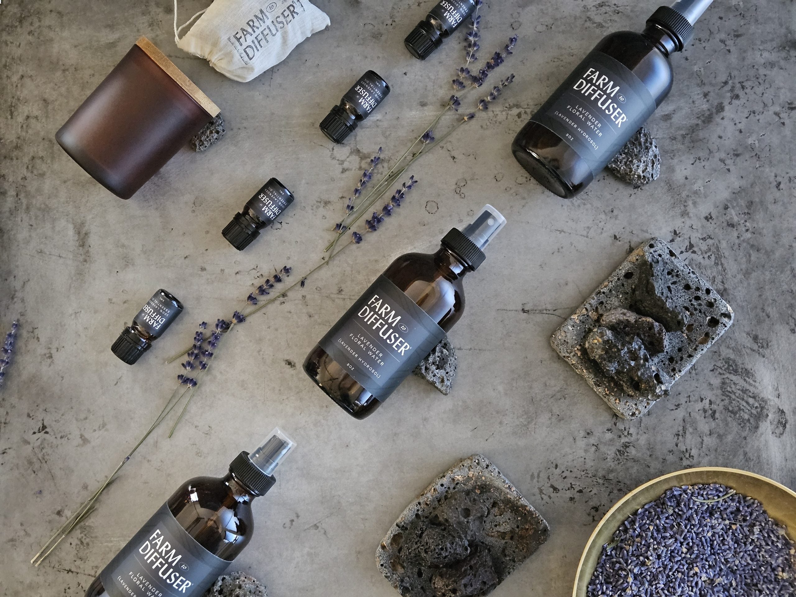 All product picture, products laying flat in diagonal lines. Volcanic Stone diffuser at the top, then lavender Essential Oil, line of lavender sprigs, lavender floral water, shower steamers, bowl of lavender buds