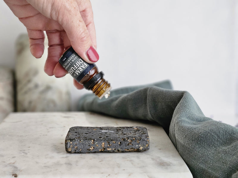 lavender essential being dropped onto a shower steamer lava stone that is set on a piece of marble with a green towel draped beside